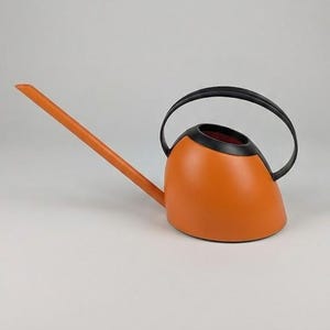 Puede incluir: Una regadera naranja con un pico largo y un asa negra. La regadera tiene un cuerpo redondeado y un borde negro alrededor de la abertura. El pico se extiende hacia la izquierda.