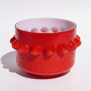 May include: A red decorative bowl with a textured exterior and a white interior. The bowl features a series of rounded, protruding accents around the exterior. The bowl is a decorative item.