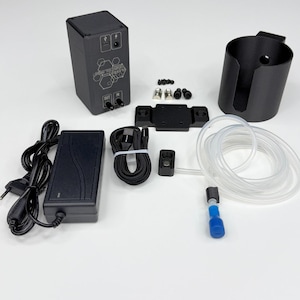 May include: A black electronic control box with a hexagonal logo, a power adapter, a black USB cable, a black cylindrical cup holder, a mounting bracket, small metal screws, and a clear plastic tube with a blue connector and a small black sensor.