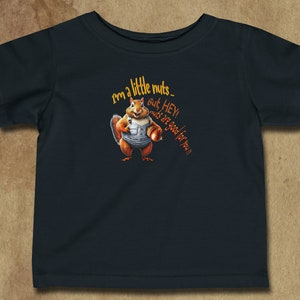 Puede incluir: Una camiseta azul oscuro con una ardilla de dibujos animados sosteniendo una nuez. La ardilla lleva un mono y el texto "I'm a little nuts. But, HEY! nuts are good for you!" está impreso en la camiseta.