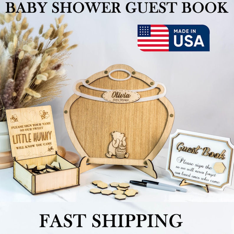 May include: Wooden Winnie the Pooh themed baby shower guest book with a honey pot shaped frame, a sign that says "Please sign your name so our sweet little hunny will know you came", and a box with wooden hearts. The sign also says "Guest Book" and "Please sign the so we will never forget our loved ones who came".