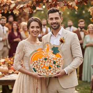 May include: A wooden pumpkin-shaped guest book featuring a clear acrylic front panel, filled with small wooden leaf-shaped cutouts for signatures. The center of the pumpkin displays the text Amanda & Robert 10.12.24, surrounded by orange and green accents.