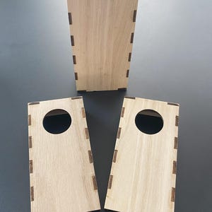 以下が含まれることがあります： 明るい茶色の未完成の木製ボックスが3つ。2つのボックスには円形の開口部があります。ボックスは濃い茶色の長方形の接合部で組み立てられています。ボックスはおそらく保管または表示用です。