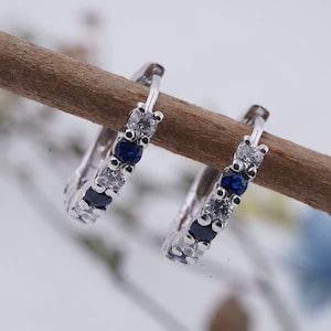 May include: A pair of silver hoop earrings with a row of clear and blue gemstones.