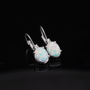 May include: A pair of silver dangle earrings with oval-shaped white opal stones and small clear cubic zirconia accents.