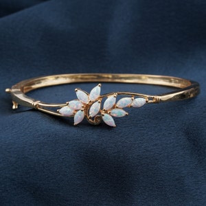 Op de afbeelding: Een gouden armband met een bloemmotief met witte opaalstenen. De armband is open en heeft een scharnier sluiting.