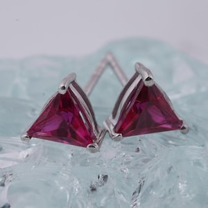 May include: A pair of silver stud earrings with triangular red ruby gemstones.