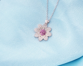 May include: A silver necklace with a flower pendant. The flower is made of white stones and has a pink center.