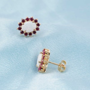 May include: A pair of gold earrings featuring a white opal gemstone set in a halo of small red gemstones.