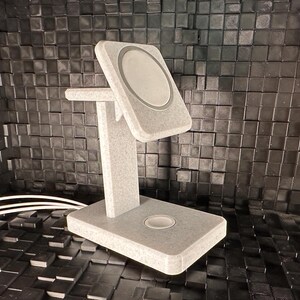 May include: A gray, textured, wireless charging stand with a circular charging pad. The stand has a raised platform for holding a phone or other device.