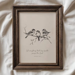 Puede incluir: Una impresión enmarcada con un dibujo de tres pájaros posados en una rama. La obra de arte es en blanco y negro, sobre un fondo beige. El marco es de color marrón oscuro, con el texto "Let everything that has breath praise the Lord!" debajo.