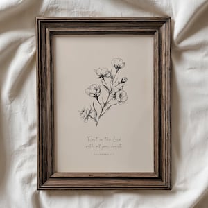 Pode incluir: Uma impressão artística emoldurada com um design floral. A impressão apresenta uma ilustração botânica a preto e branco de flores e folhas sobre um fundo bege. A moldura castanha escura tem um acabamento texturizado. O texto diz: "Confie no Senhor de todo o seu coração."