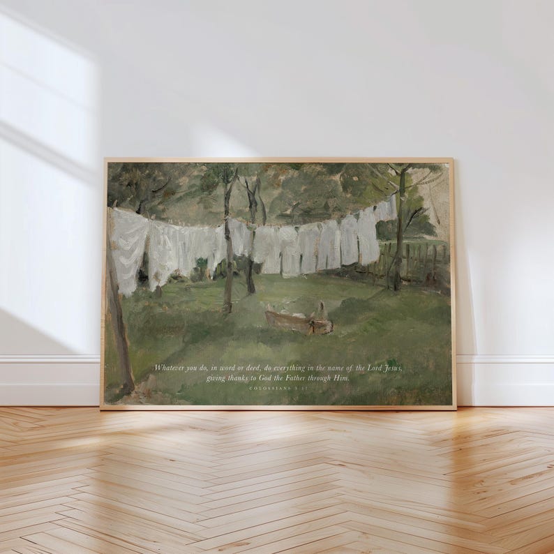 May include: A framed print of a pastoral scene with white laundry hanging on a clothesline. The artwork features a green landscape with trees and a small boat. Text at the bottom reads, "Whatever you do, in word or deed, do everything in the name of the Lord Jesus, giving thanks to God the Father through Him."