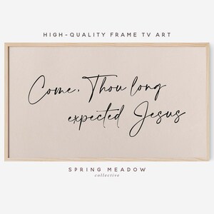 May include: A framed print with a beige background and black cursive text that reads "Come. Thou long expected Jesus." The print is framed in a light wood frame. The text "SPRING MEADOW collective" is printed below the cursive text.