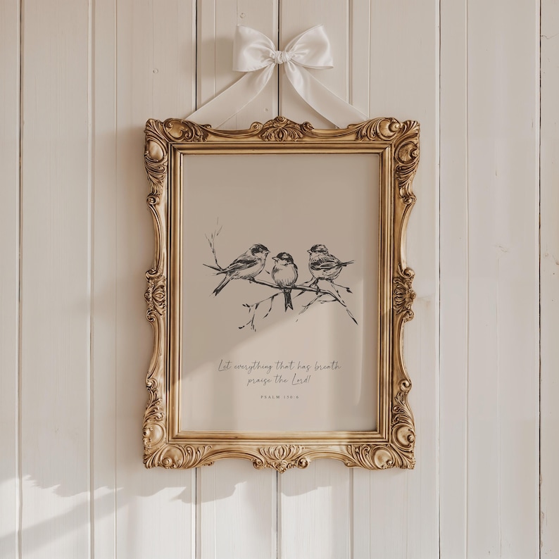 May include: A framed print featuring a detailed illustration of three birds perched on a branch. The artwork is in black and white, set against a beige background, and framed in an ornate gold frame. The print is adorned with a white bow and includes the text "Let everything that has breath praise the Lord!" and "Psalm 150:6".