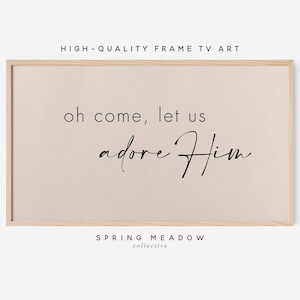 May include: A framed print with a beige background and black text that reads "oh come, let us adore Him". The print is framed in a light wood frame. The text "SPRING MEADOW collective" is printed below the main text.