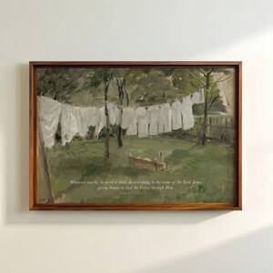 May include: A framed print of a pastoral scene. White laundry hangs on a clothesline in a green field. The artwork has a brown wooden frame and includes text at the bottom: "Whatever you do, in word or deed, do everything in the name of the Lord Jesus, giving thanks to God the Father through Him."
