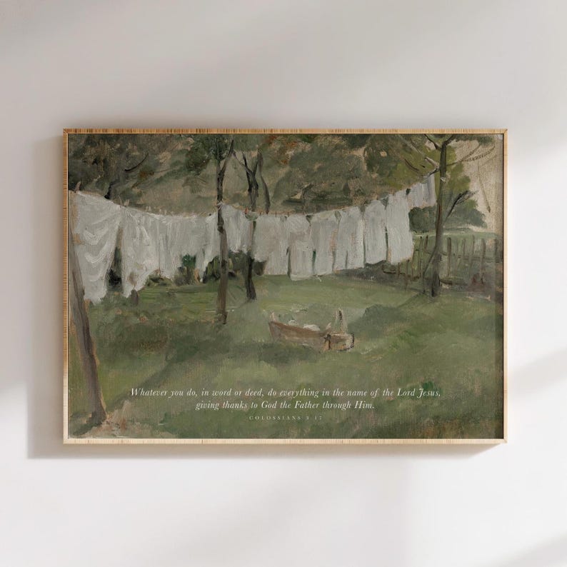 May include: A framed art print depicting a pastoral scene with white laundry hanging on a clothesline. The artwork features a green field, trees, and a small boat. The text reads: "Whatever you do, in word or deed, do everything in the name of the Lord Jesus, giving thanks to God the Father through Him."