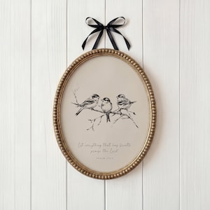 May include: An oval-shaped framed print featuring a black and white illustration of three birds perched on a branch. The frame is gold with a beaded edge, and a black ribbon is attached for hanging. The print includes the text "Let everything that has breath praise the Lord!" and "Psalm 150:6."