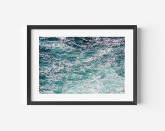 Op de afbeelding: Een close-up foto van een stormachtige zee met schuimkoppen en turquoise water.