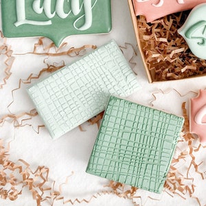 May include: A collection of six decorated sugar cookies in a box. The cookies are decorated with green and pink icing and have names written on them, including "Lucy", "Sophie", "Maddi", "Sammie", and "Jackie".