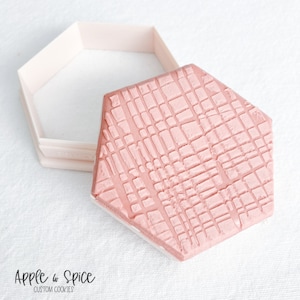 May include: A pink hexagonal cookie cutter with a geometric pattern. The cutter is made of plastic and is designed for making cookies.