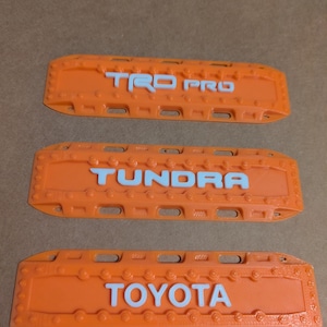 May include: Three orange plastic license plate frames with white lettering. The top frame says "TRD PRO", the middle frame says "TUNDRA", and the bottom frame says "TOYOTA".