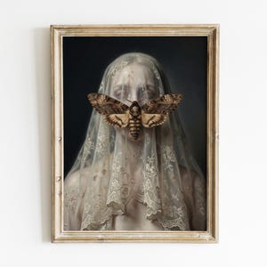 May include: A framed print featuring a portrait of a person veiled in lace, with a large moth covering the face. The moth has a skull-like pattern on its body. The frame is a light, antique gold color.