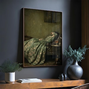 May include: A framed wall art print depicting a person in a long, flowing sage green gown with intricate gold floral embroidery, reclining on a dark curved sofa. A small side table holds a glass of amber liquid and a single white flower.