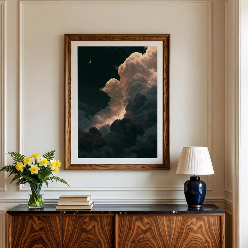 May include: A framed vertical wall art print depicting a night sky filled with voluminous, dark, and illuminated clouds. A thin crescent moon is visible in the upper left corner against a deep black background. The print is enclosed in a wooden frame.