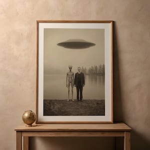 Puede incluir: Impresi&oacute;n enmarcada en tonos sepia que representa a un hombre con traje y un extraterrestre de pie, con un platillo volante encima. La escena est&aacute; ambientada junto a un lago con &aacute;rboles al fondo, creando una atm&oacute;sfera surrealista y misteriosa.