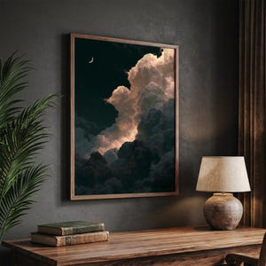 May include: A framed wall art print depicting a night sky with a crescent moon and stars above large, voluminous clouds. The clouds are illuminated with soft, warm light against a dark, deep blue background, creating a dramatic contrast.