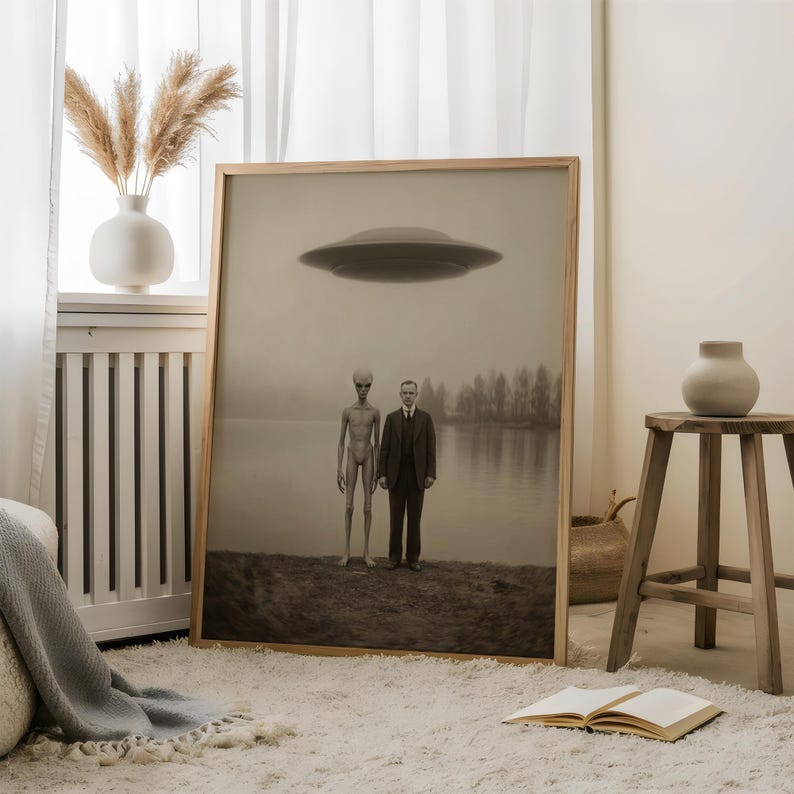 Puede incluir: Una impresi&oacute;n enmarcada en tonos sepia representa a un hombre con traje junto a un extraterrestre, con un OVNI sobre un lago. La obra de arte se exhibe en una habitaci&oacute;n con una alfombra blanca, un jarr&oacute;n y un taburete de madera.