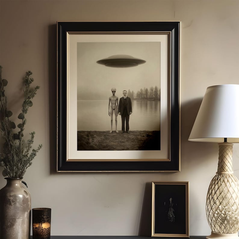 Puede incluir: Impresi&oacute;n enmarcada en tonos sepia que representa un OVNI sobre un lago, con un extraterrestre y un hombre con traje en la orilla. La obra de arte est&aacute; en un marco negro y dorado, complementada con una l&aacute;mpara y otros elementos decorativos.