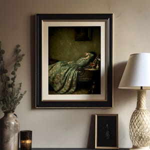 May include: A framed wall art print featuring a painting of a person reclining on a dark chaise lounge, wearing a long, flowing green gown with intricate gold embroidery. The artwork is encased in a black frame with a cream-colored mat border.