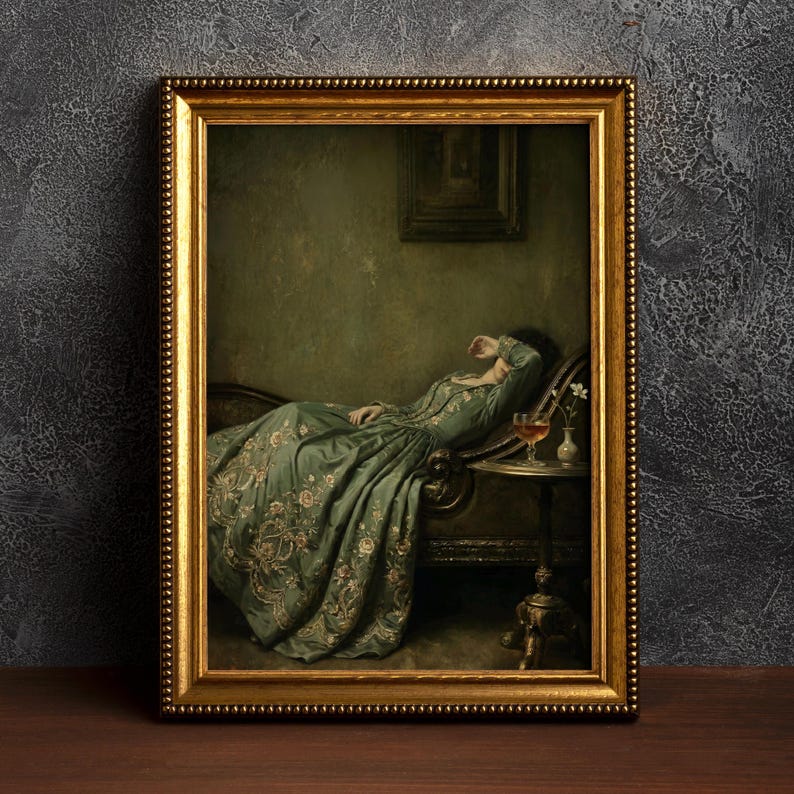 May include: A framed wall art print depicting a person in a long, sage green dress with floral embroidery reclining on a chaise lounge. The person has an arm raised to their face. A small side table holds a glass of liquid and a single white flower.
