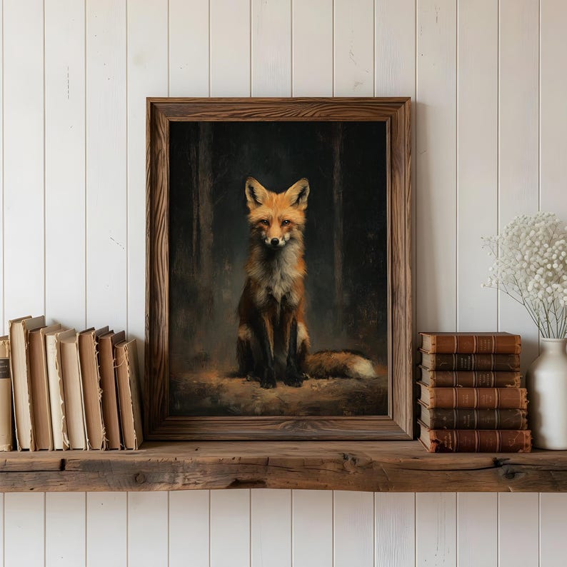 May include: A framed artwork featuring a fox with orange and white fur, set against a dark forest backdrop. The fox is sitting upright, with a focused gaze. The frame is a dark brown color. The artwork is displayed on a wooden shelf with books.
