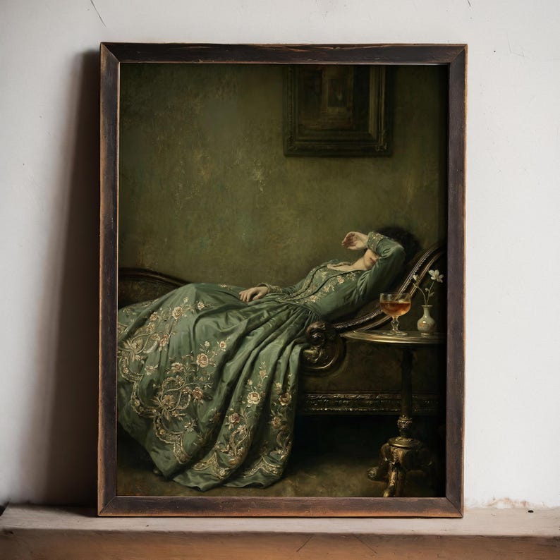 May include: A framed oil painting print depicting a person reclining on a dark chaise lounge, wearing a long, sage green gown with intricate floral embroidery. A small pedestal table holds a glass of amber liquid and a tiny vase with white flowers.