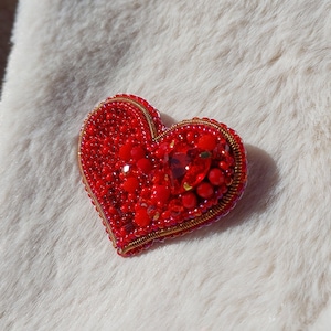 Könnte beinhalten: Eine rote, herzförmige Brosche mit goldenen Drahtverzierungen.
