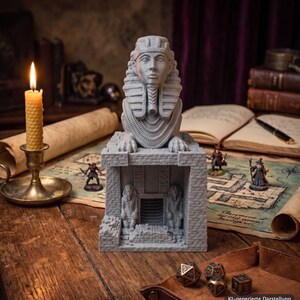 Könnte beinhalten: Eine graue, 3D-gedruckte Sphinx-Statue mit detailliertem Pharaonenkopf und Kopfschmuck, platziert auf einem steinstrukturierten Tempelsockel mit zwei kleineren Statuen, die einen zentralen Eingang flankieren, alles in matter Optik.