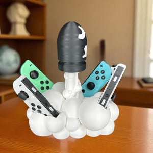 May include: A white and black rocket-shaped controller holder with a black bullet-shaped top and white accents. The holder is designed to hold four game controllers, with green, blue, and white controllers visible.