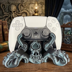 Könnte beinhalten: Ein weiß-grauer PlayStation 5-Controller ruht auf einem teal-farbenen, schädelartigen Ständer mit tentakelartigen Armen. Der Ständer steht auf einer Holzoberfläche, mit einem Vintage-Hintergrund.