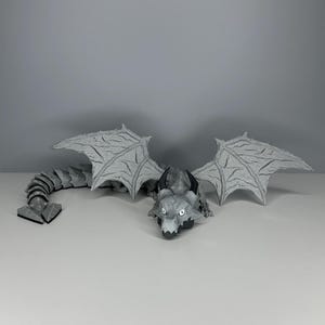 May include: A gray dragon figurine with black eyes and wings. The dragon has a long, segmented tail.