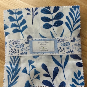 May include: A stack of fabric squares with a white background and blue botanical leaf patterns. A band with the text "Blissful Blues" wraps around the squares. The fabric is likely for quilting or crafting projects.