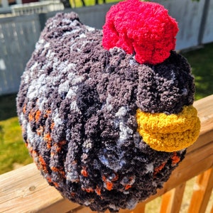 Puede incluir: Un juguete de peluche de pollo tejido a crochet con un cuerpo estampado en negro, blanco, naranja y gris, un pico amarillo y una cresta rosa brillante.