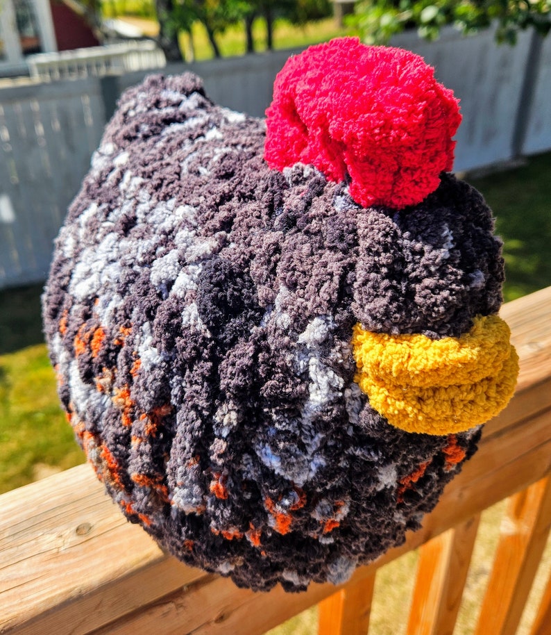 Puede incluir: Un juguete de peluche de pollo tejido a crochet con un cuerpo estampado en negro, blanco, naranja y gris, un pico amarillo y una cresta rosa brillante.
