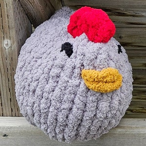 Puede incluir: Un juguete de peluche de pollo de crochet gris con un pomp&oacute;n rojo en la parte superior de la cabeza, un pico amarillo y ojos negros.
