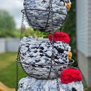 Puede incluir: Tres adornos de pollo de crochet colgando de una cadena de metal en una cesta de alambre. Los pollos son blancos, negros y grises con detalles rojos y amarillos. El texto "3 opciones de tama&ntilde;o" y "2 opciones de plumas" es visible en la imagen.