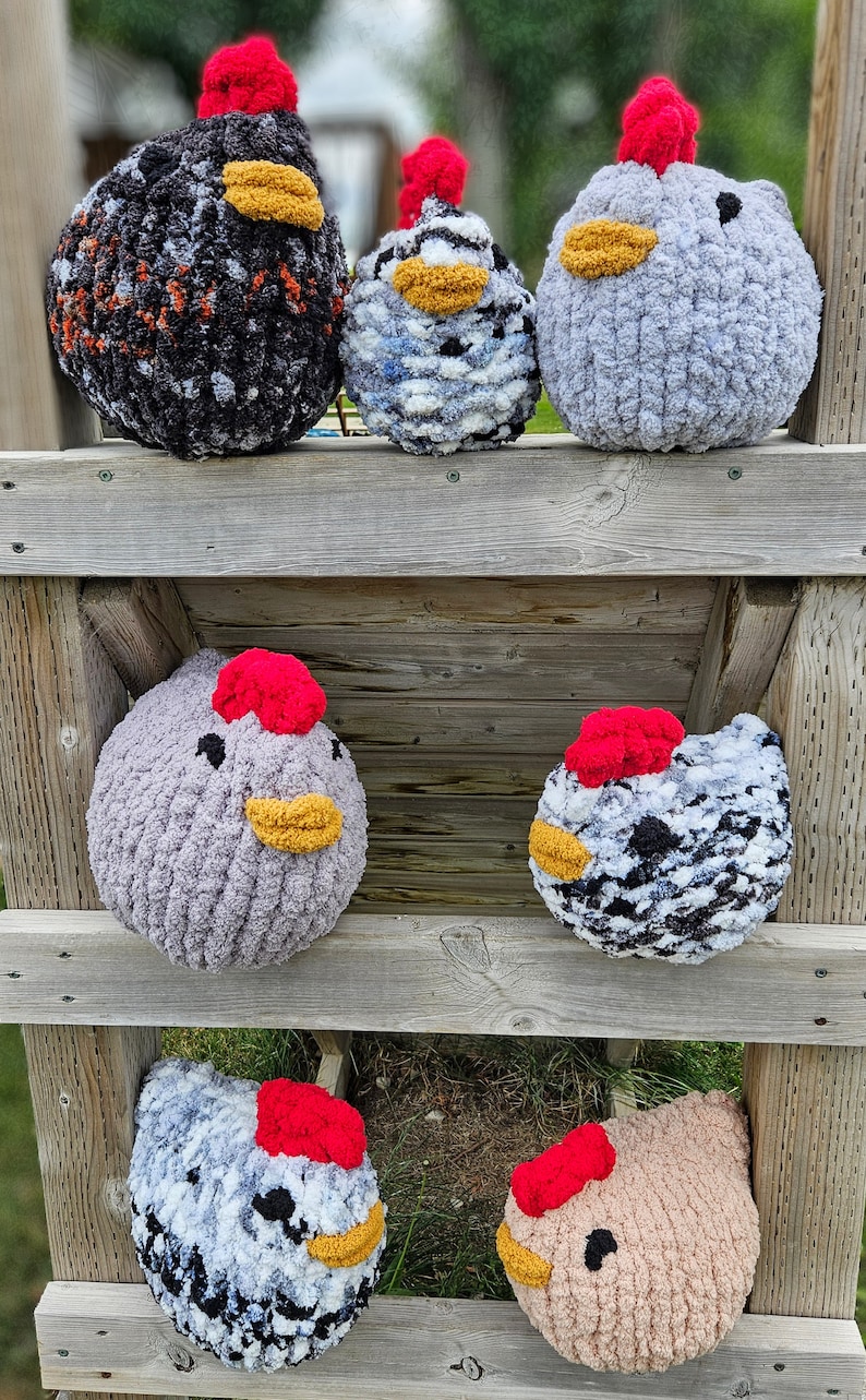 Puede incluir: Seis peluches de pollo tejidos a crochet en varios colores y patrones, incluyendo blanco y negro, gris y beige, dispuestos en un estante de madera.