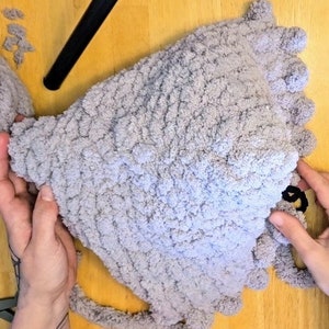 Puede incluir: Un gorro de punto de color gris con una superficie texturizada y un pomp&oacute;n en la parte superior.